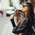 stylish girl smoking an e-cigarette as she is walking through the city